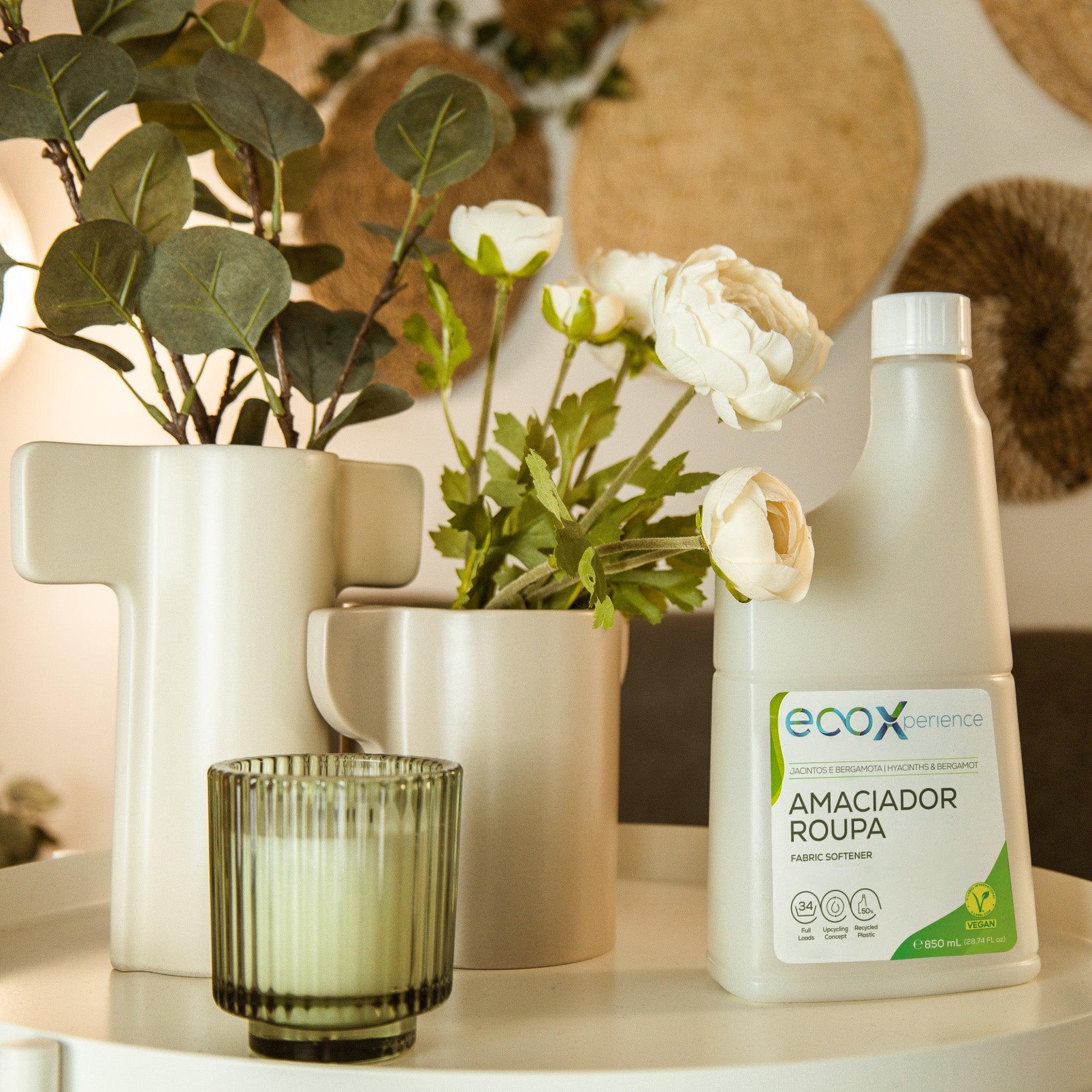 Embalagem de amaciador da roupa Jacintos e Bergamota EcoX 850mL ao lado de uma vela e de plantas