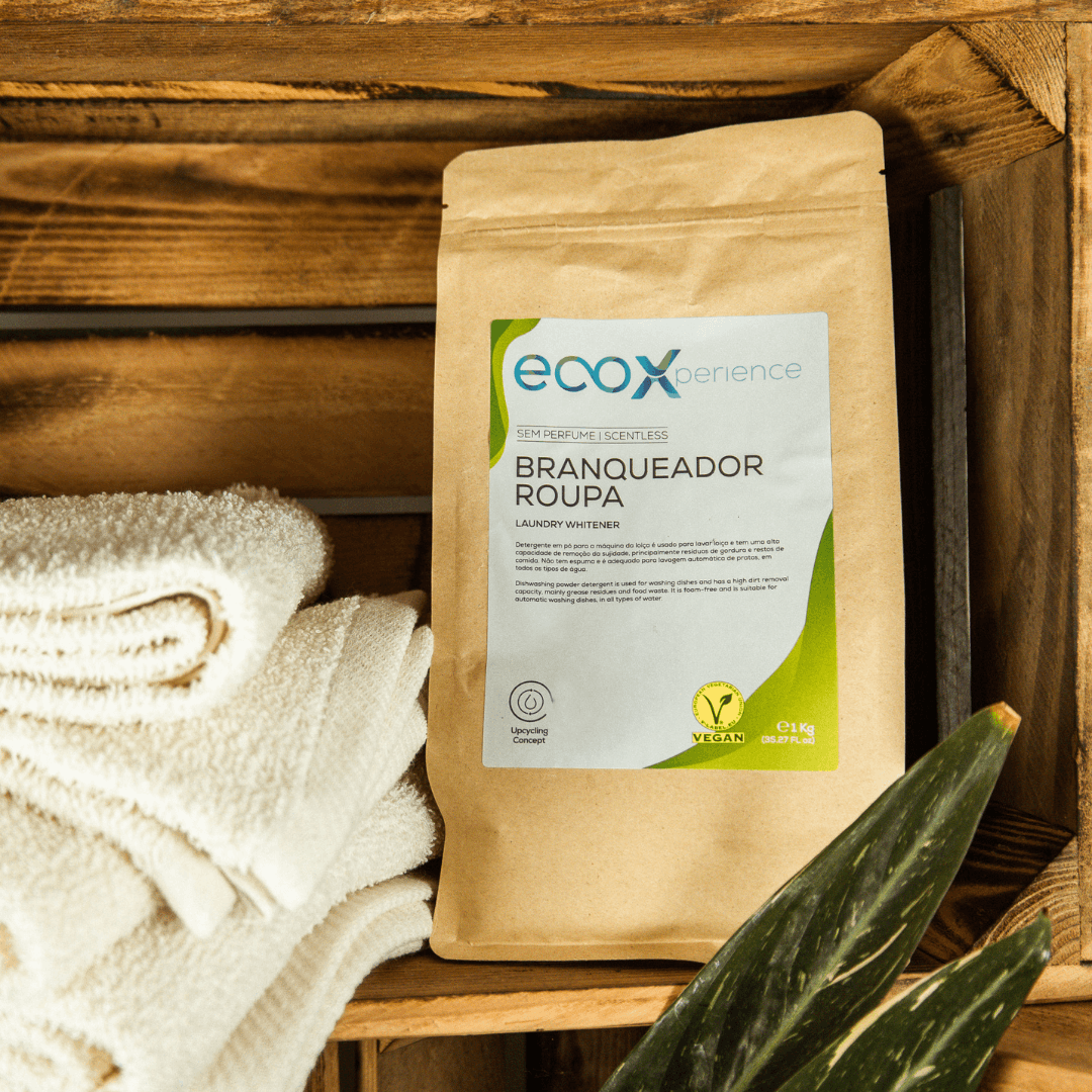 Embalagem de branqueador de roupa EcoX 1kg numa prateleira de madeira com toalhas ao lado