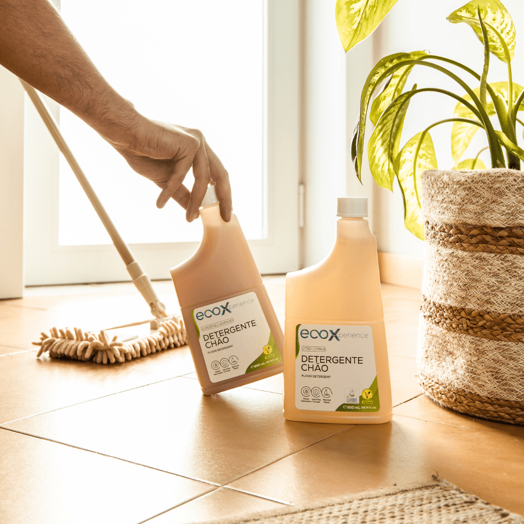 Mão a agarrar a embalagem de detergente chão alfazema EcoX 850mL, que está ao lado de embalagem de Detergente chão citro EcoX 850mL