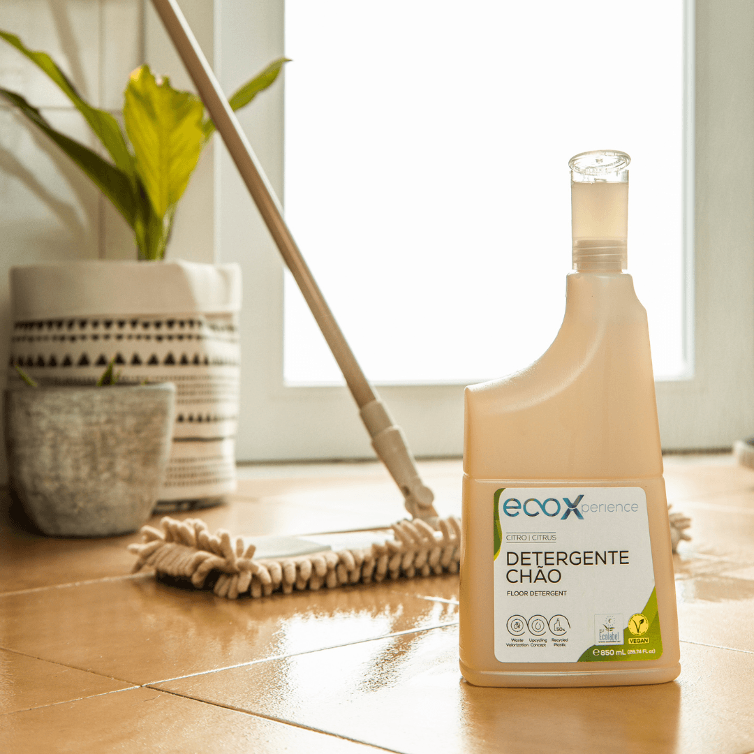 Embalagem de detergente chão citro EcoX 850mL com doseador de detergente, ao lado de uma esfregona