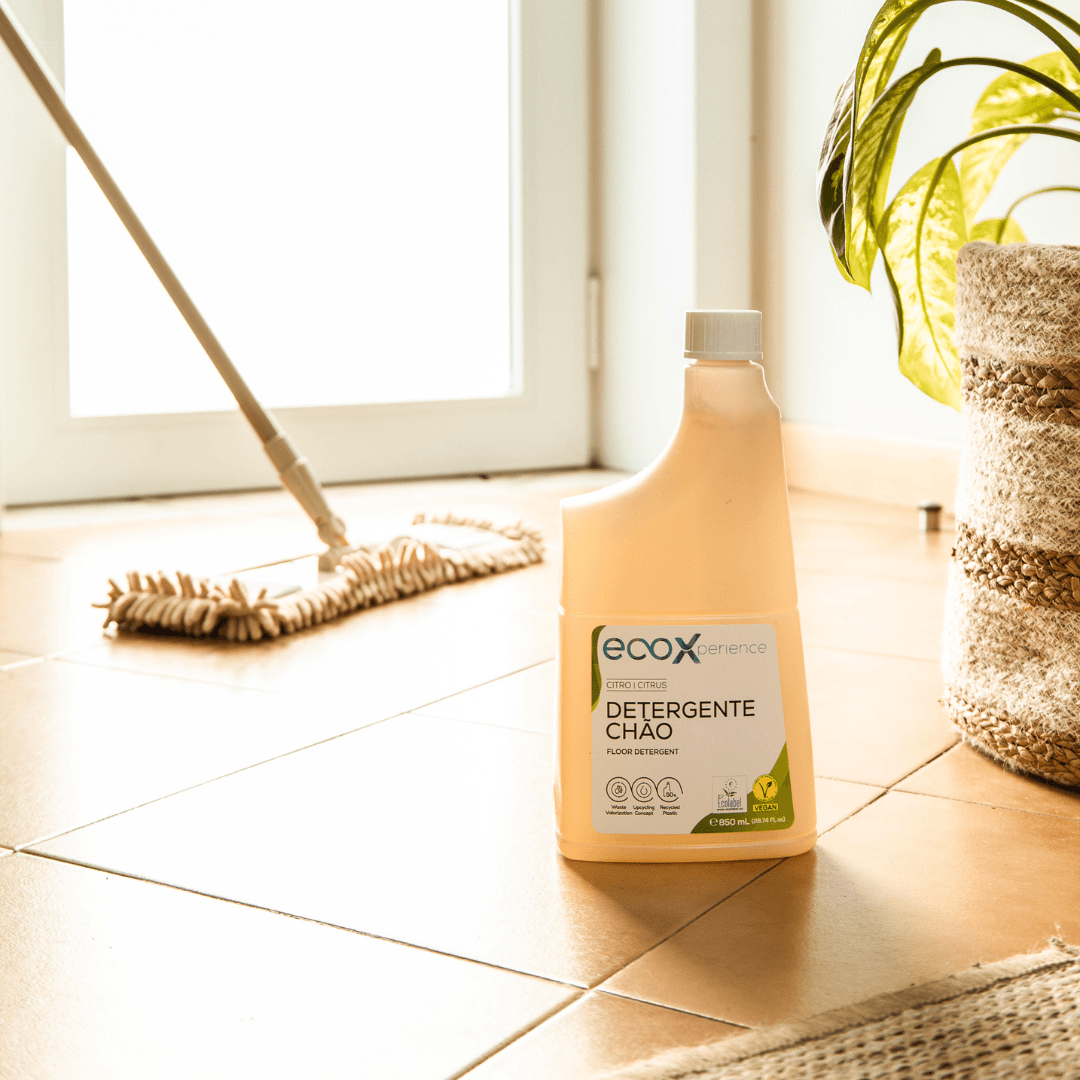 Embalagem de detergente chão citro EcoX 850mL ao lado da esfregona e de uma planta