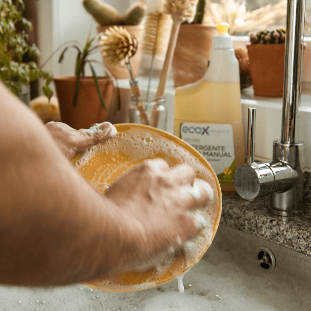 Mãos a lavar um prato, com embalagem de detergente loiça EcoX 850mL ao fundo