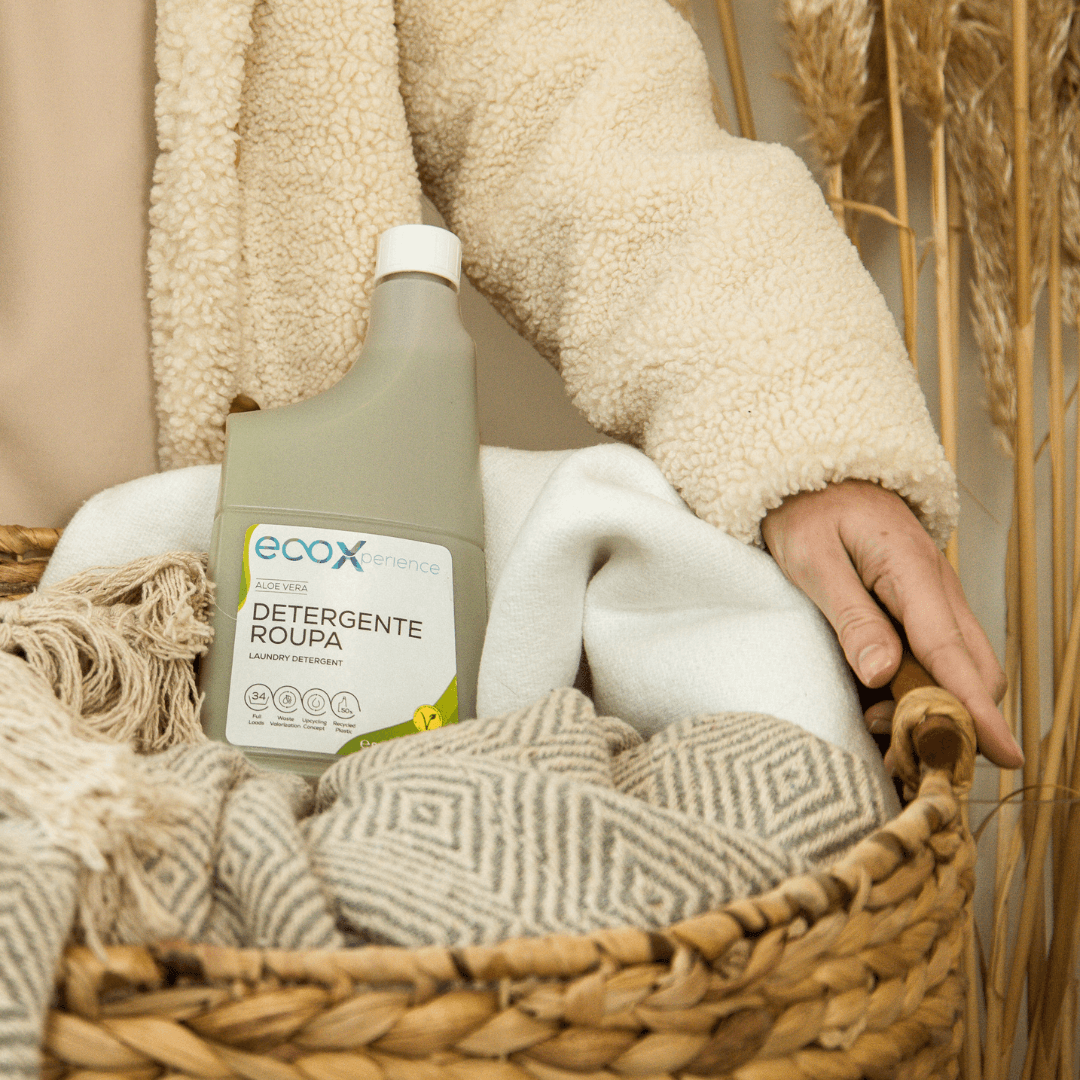 Mão de pessoa a agarrar um cesto com roupa e com uma embalagem de detergente roupa aloe vera EcoX 850mL