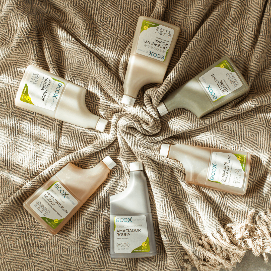 Embalagem de detergente roupa delicada EcoX 850mL, ao lado de outros detergentes EcoX que estão em círculo em cima de uma manta