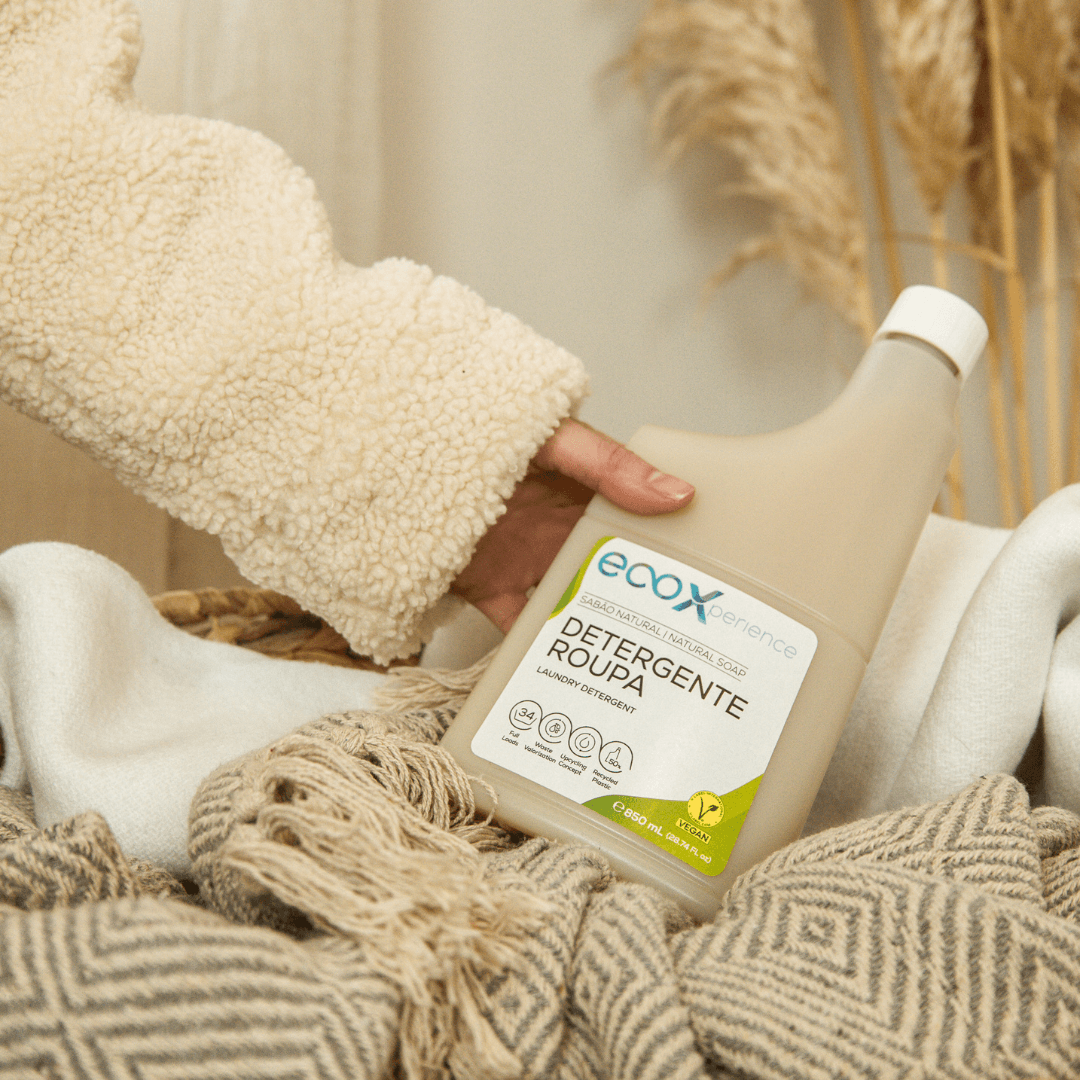 Mão a segurar uma embalagem de detergente roupa sabão natural EcoX 850mL que está num cesto em cima da roupa