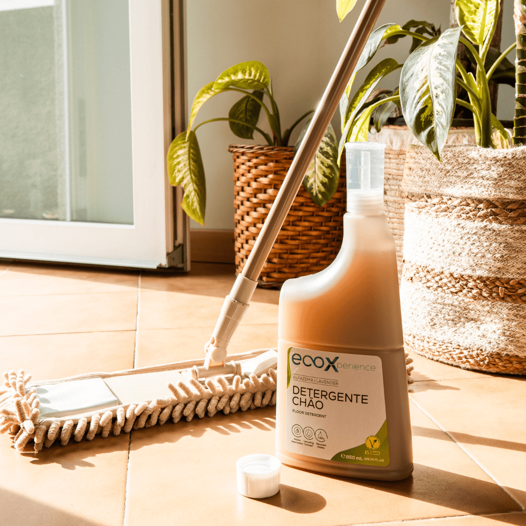 Embalagem de detergente chão alfazema EcoX 850mL com doseador de detergente, ao lado da esfregona e plantas