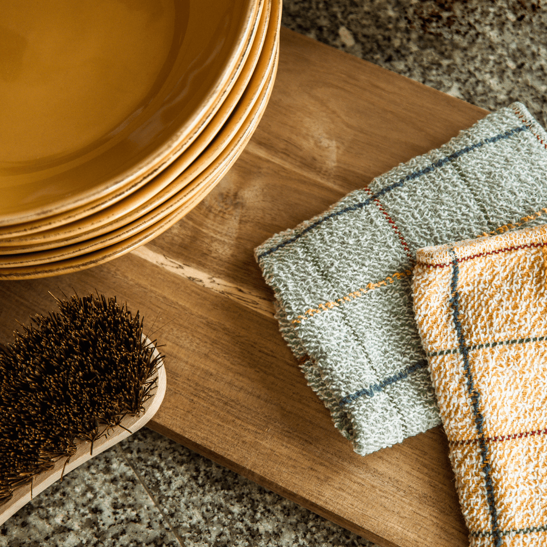 Panos da loiça EcoX ao lado de pratos e de uma escova